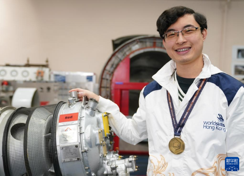 在香港专业教育学院，黄富东佩戴着“2024年里昂世界技能大赛”飞机维修项目的铜牌和涡轮螺旋桨飞机引擎合影（1月14日摄）。