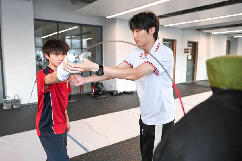 ↑图为广东现代五项运动协会教练员肖勇炫（右）纠正广州市中黄港澳子弟学校港籍生张嗣涛击剑技术细节（6月19日摄）。