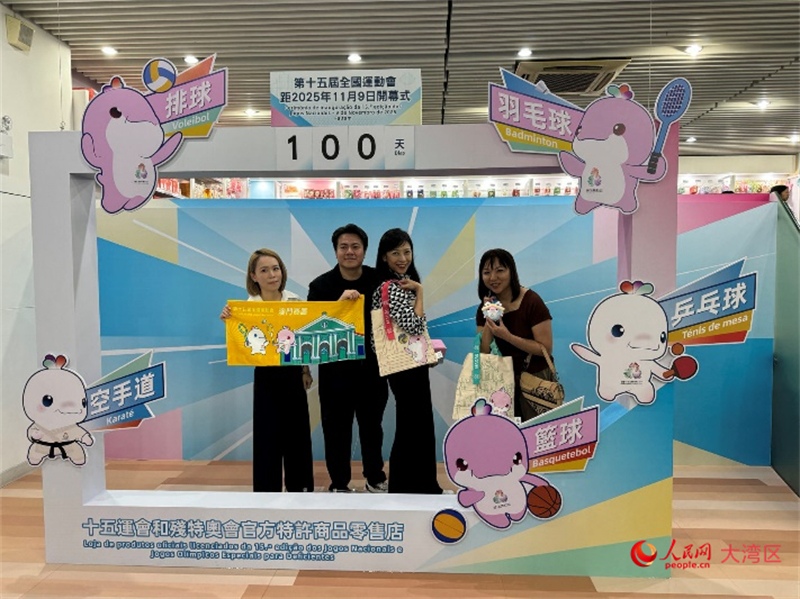 图为特许商品零售店顾客与十五运会开幕倒计时牌合影。